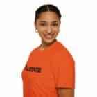A person is smiling and facing forward against a white background while wearing a Failstate Softstyle T-shirt in orange.